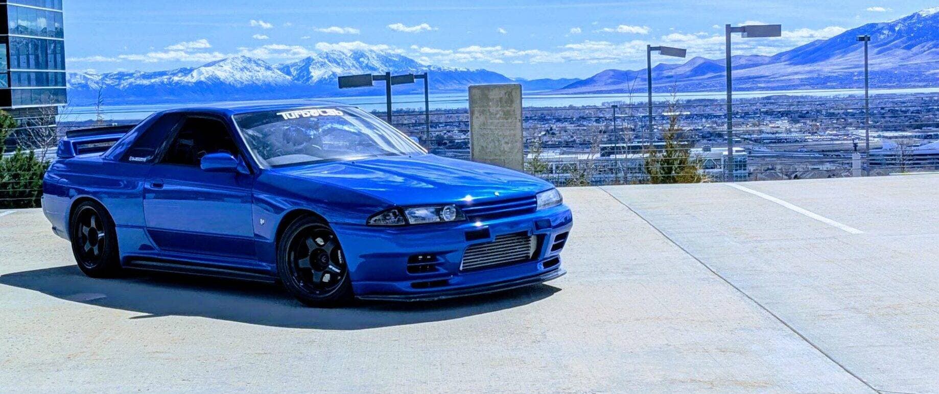 Josh's blue R32 Nissan Skyline project car with a Turbo Lab windshield banner, snowy Wasatch mountains behind